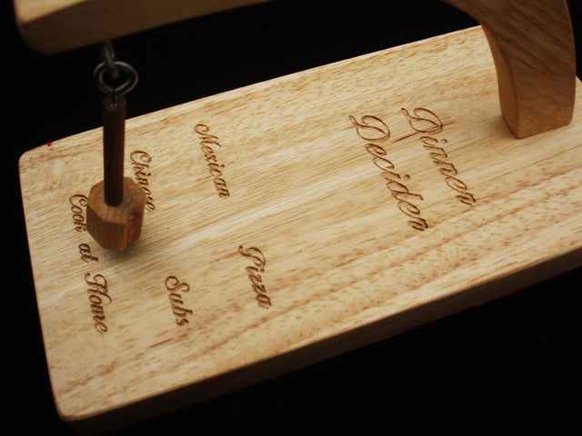Dinner Decider face laser engraved with Mexican, Chinese, Pizza, Subs and Cook at Home, the wooden pendulum hanging beside Chinese, on a black backdrop