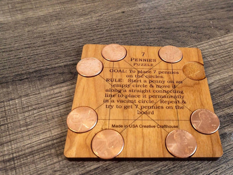 7 Pennies Puzzle by Creative Crafthouse on a wooden table: a square cherry-finished board with its goal and rules engraved in the center and seven pennies resting on its eight circles.