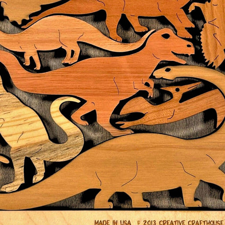 Close-up of the Dinosaur Dilemma wooden puzzle by Creative Crafthouse: dinosaur pieces in several wood tones, including a long-necked sauropod and a T. rex, above the frame's engraved edge.