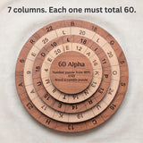 Top view of the 60 Alpha puzzle on linen showing seven columns of numbers and letters across the base and three rings. Headline: 7 columns. Each one must total 60.