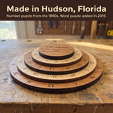 The 60 Alpha puzzle on a worn wooden workbench. Headline: Made in Hudson, Florida. Number puzzle from the 1890s. Word puzzle added in 2019.