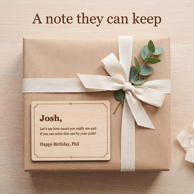 Engraved wood message card with a birthday message resting on a gift wrapped in kraft paper with a cream ribbon and eucalyptus