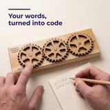 Hands turning a gear on the Enigma II Small and writing the coded letters on a notepad, with the headline Your words, turned into code.