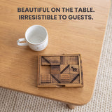 The Get My Goat wooden sliding block puzzle mid-game on a light oak coffee table beside a white coffee mug, its engraved raintree blocks showing the goat silhouette, the USA patent 1914 maker inscription and the instruction to move the goat inside the octagon. Headline: Beautiful on the table. Irresistible to guests.