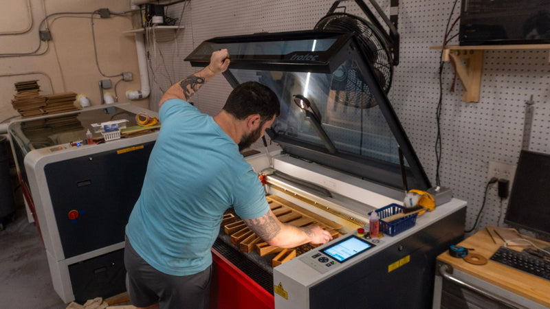 Justin standing over a laser machine preparing a add a personalized laser engraving to some Penny Drop games.
