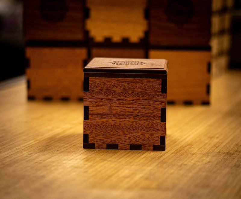 Wooden puzzle box on a wooden surface with blurred stacks of similar boxes in the background.