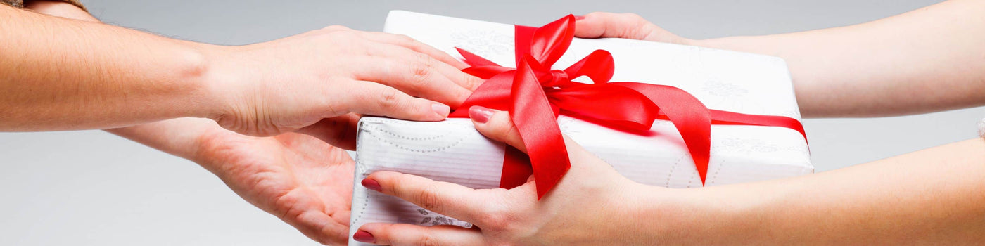 Two pairs of hands exchanging a gift with puzzles and games inside wrapped in white paper with a red ribbon.