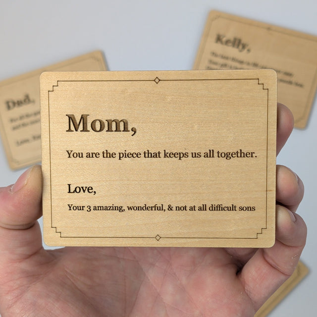 Hand holding a Wood Message Card to show its 4 by 3 inch size, engraved with the example message You are the piece that keeps us all together
